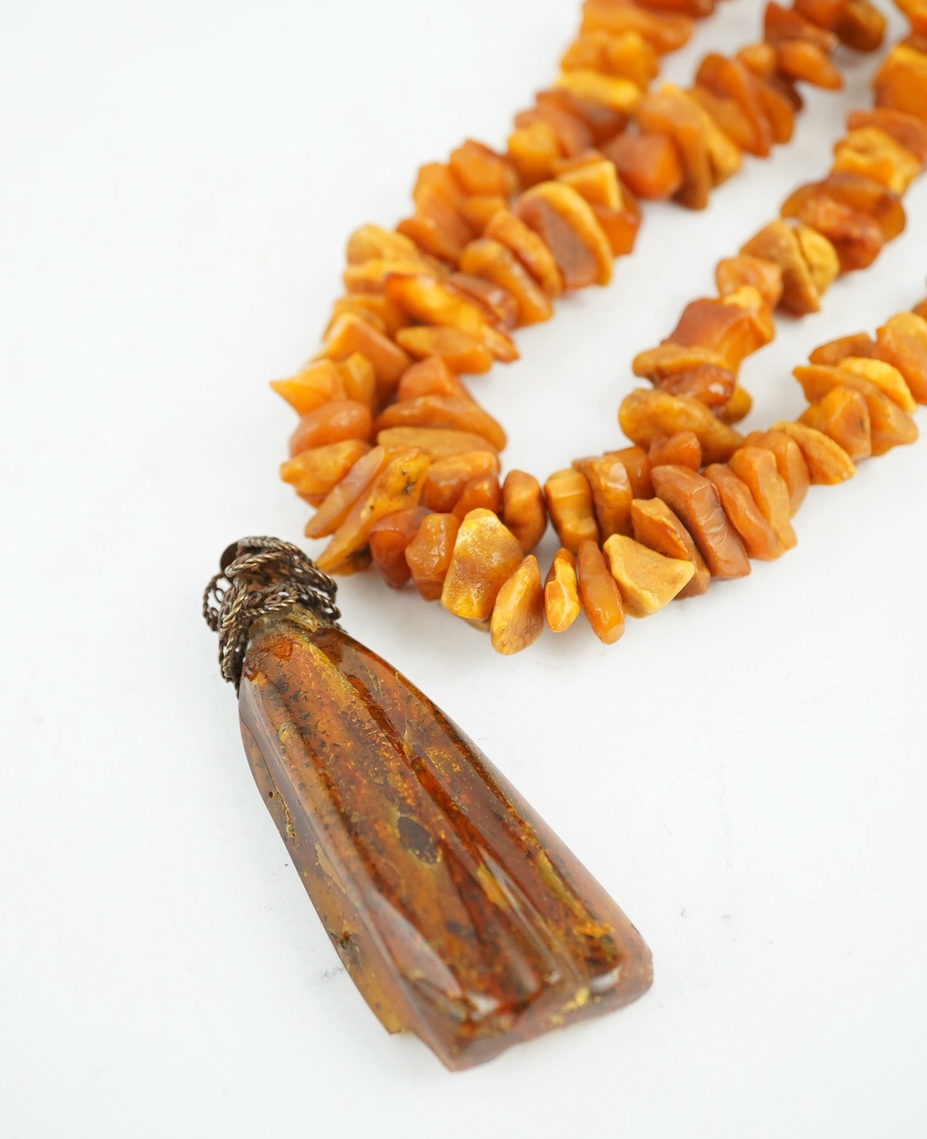 A long single strand unpolished amber necklace, 162cm and a gilt metal mounted amber pendant, gross weight 205 grams. Condition - fair